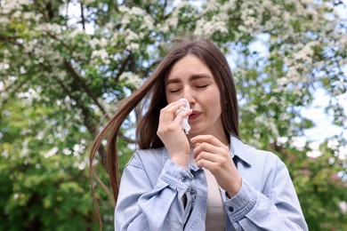 Photo of Woman with paper tissue suffering from seasonal pollen allergy near blossoming tree on spring day, space for text