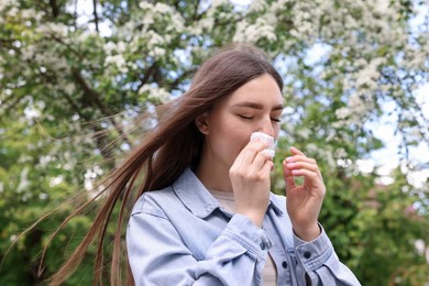 Photo of Woman with paper tissue suffering from seasonal pollen allergy near blossoming tree on spring day