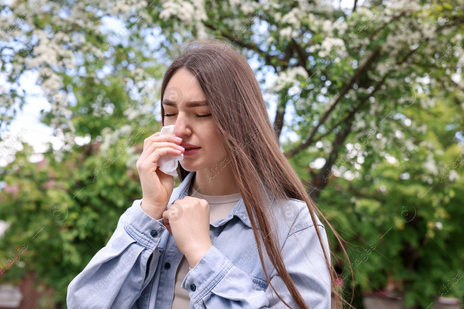 Woman with paper tissue suffering from seasonal pollen allergy near blossoming tree on spring day Photo of Woman with paper tissue suffering from seasonal pollen allergy near blossoming tree on spring day