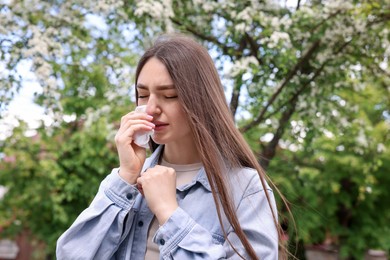 Photo of Woman with paper tissue suffering from seasonal pollen allergy near blossoming tree on spring day