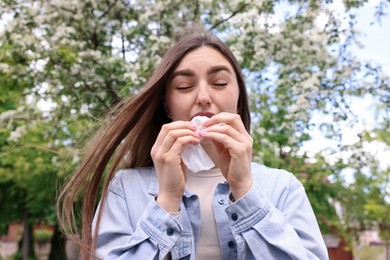 Photo of Woman with paper tissue suffering from seasonal pollen allergy near blossoming tree on spring day