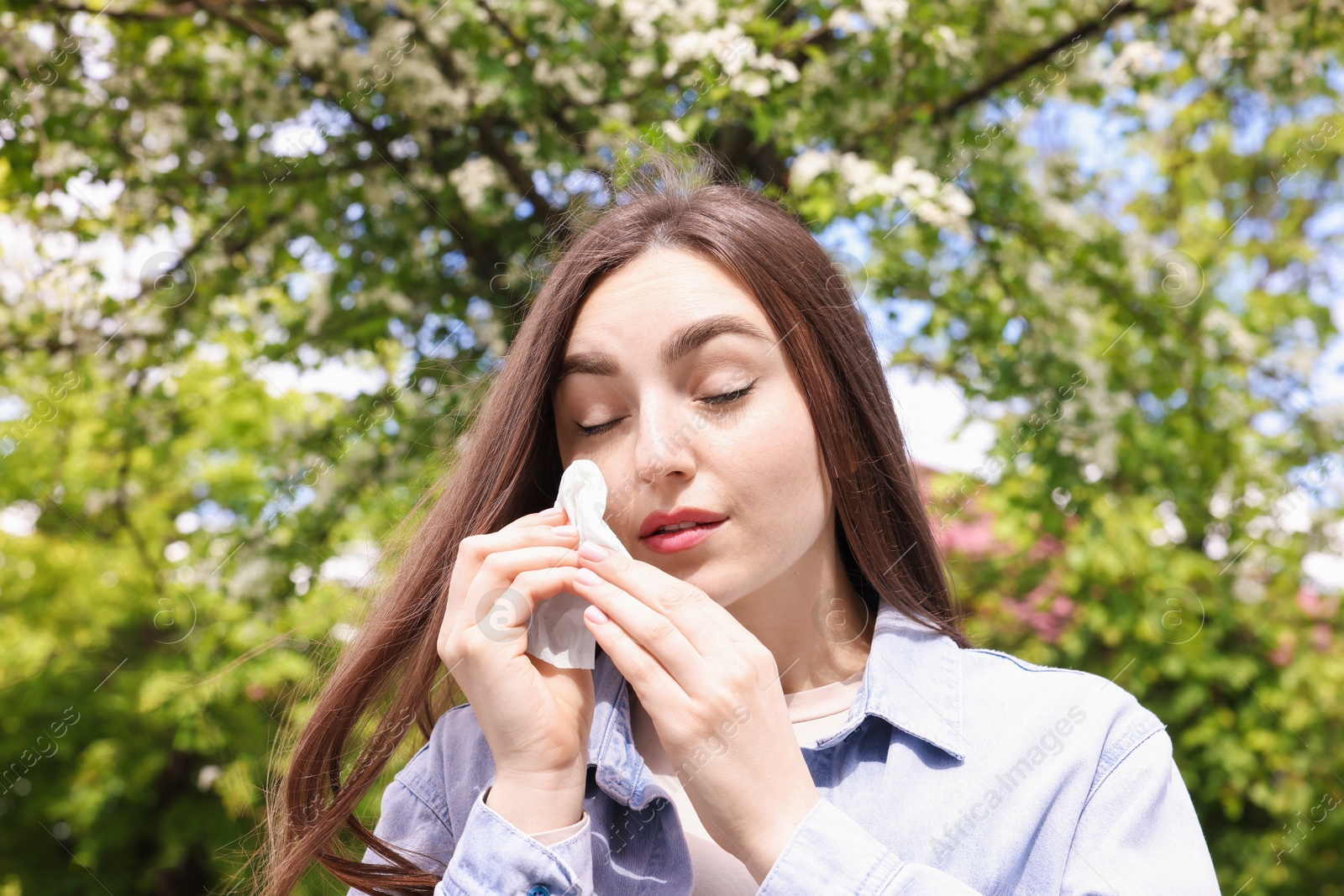 Woman with paper tissue suffering from seasonal pollen allergy near blossoming tree on spring day Photo of Woman with paper tissue suffering from seasonal pollen allergy near blossoming tree on spring day