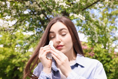 Photo of Woman with paper tissue suffering from seasonal pollen allergy near blossoming tree on spring day