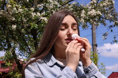 Photo of Woman with paper tissue suffering from seasonal pollen allergy near blossoming tree on spring day