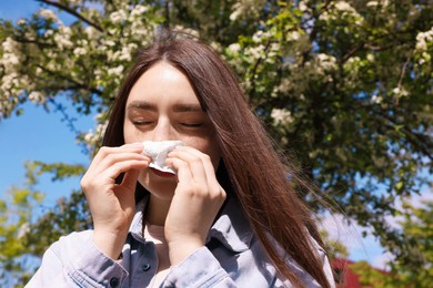 Photo of Woman with paper tissue suffering from seasonal pollen allergy near blossoming tree on spring day
