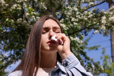 Photo of Woman with paper tissue suffering from seasonal pollen allergy near blossoming tree on spring day, low angle view