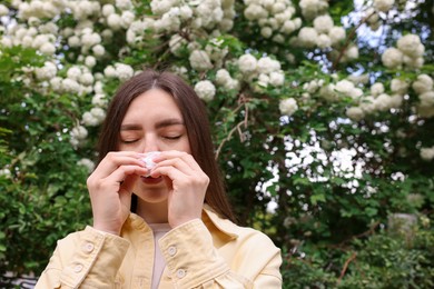 Photo of Woman with paper tissue suffering from seasonal pollen allergy near blossoming shrub on spring day, space for text