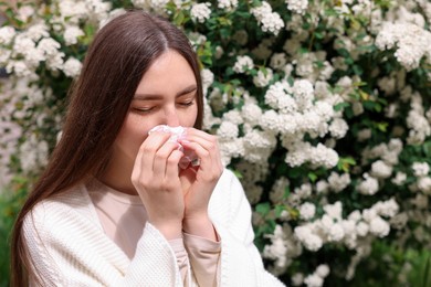 Photo of Woman with paper tissue suffering from seasonal pollen allergy near blossoming shrub on spring day, space for text