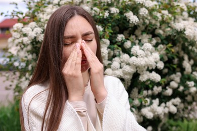 Photo of Woman suffering from seasonal pollen allergy near blossoming shrub on spring day, space for text