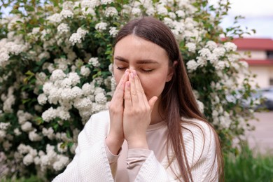 Photo of Woman suffering from seasonal pollen allergy near blossoming shrub on spring day