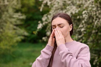 Photo of Woman suffering from seasonal pollen allergy near blossoming shrub on spring day, space for text