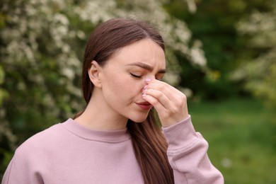 Photo of Woman suffering from seasonal pollen allergy near blossoming shrub on spring day