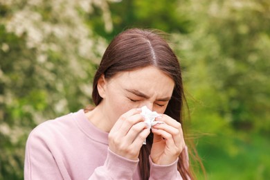Photo of Woman with paper tissue suffering from seasonal pollen allergy near blossoming shrub on spring day
