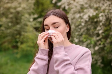 Photo of Woman with paper tissue suffering from seasonal pollen allergy near blossoming shrub on spring day