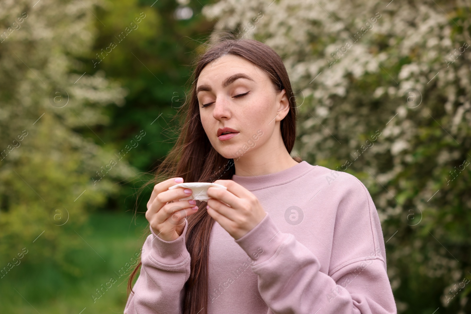 Woman with paper tissue suffering from seasonal pollen allergy near blossoming shrub on spring day Photo of Woman with paper tissue suffering from seasonal pollen allergy near blossoming shrub on spring day