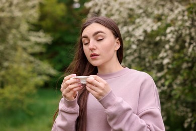 Photo of Woman with paper tissue suffering from seasonal pollen allergy near blossoming shrub on spring day