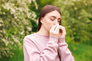 Photo of Woman with paper tissue suffering from seasonal pollen allergy near blossoming shrub on spring day