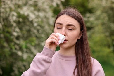 Photo of Woman with paper tissue suffering from seasonal pollen allergy near blossoming shrub on spring day