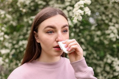 Photo of Woman with paper tissue suffering from seasonal pollen allergy near blossoming shrub on spring day