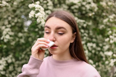 Photo of Woman with paper tissue suffering from seasonal pollen allergy near blossoming shrub on spring day