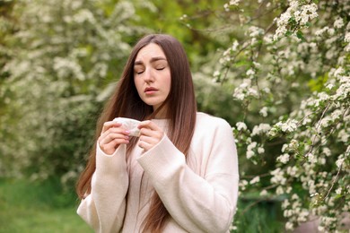 Photo of Woman with paper tissue suffering from seasonal pollen allergy near blossoming shrub on spring day