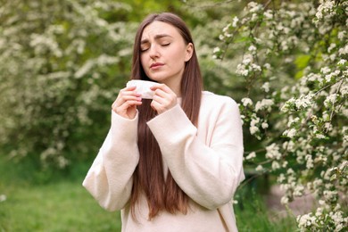 Photo of Woman with paper tissue suffering from seasonal pollen allergy near blossoming shrub on spring day