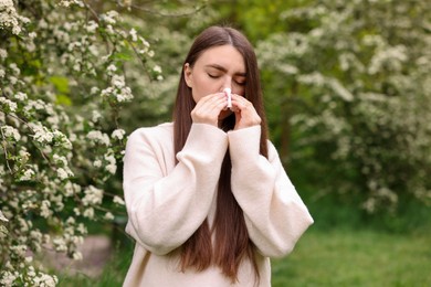 Photo of Woman with paper tissue suffering from seasonal pollen allergy near blossoming shrub on spring day