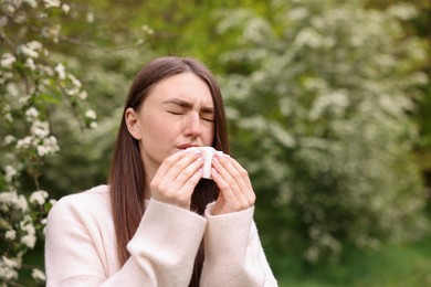 Photo of Woman with paper tissue suffering from seasonal pollen allergy near blossoming shrub on spring day, space for text
