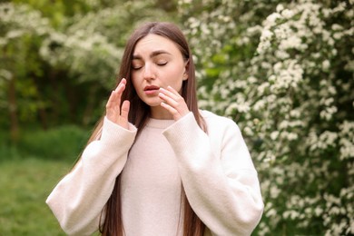 Photo of Woman suffering from seasonal pollen allergy near blossoming shrub on spring day