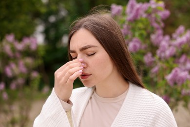 Photo of Woman suffering from seasonal pollen allergy near blossoming shrub on spring day