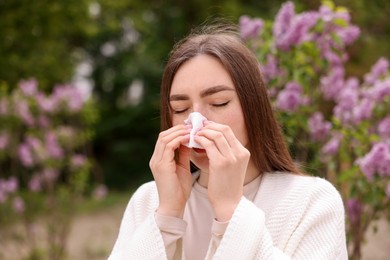 Photo of Woman with paper tissue suffering from seasonal pollen allergy near blossoming shrub on spring day, space for text