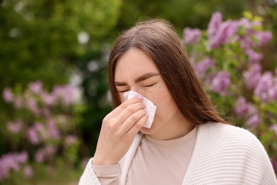 Photo of Woman with paper tissue suffering from seasonal pollen allergy near blossoming shrub on spring day, space for text