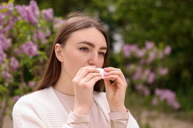 Photo of Woman with paper tissue suffering from seasonal pollen allergy near blossoming shrub on spring day, space for text