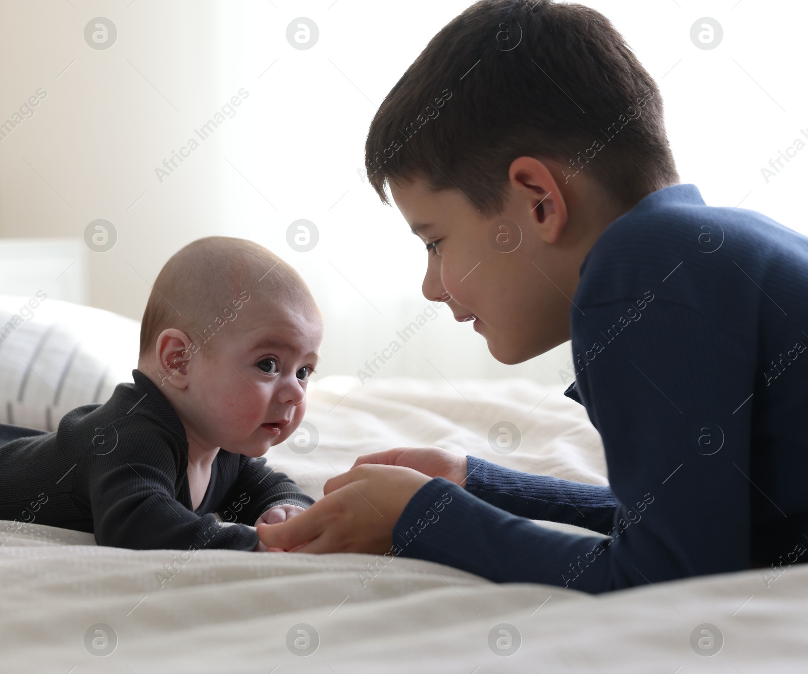 Cute little brothers holding hands on bed at home Photo of Cute little brothers holding hands on bed at home