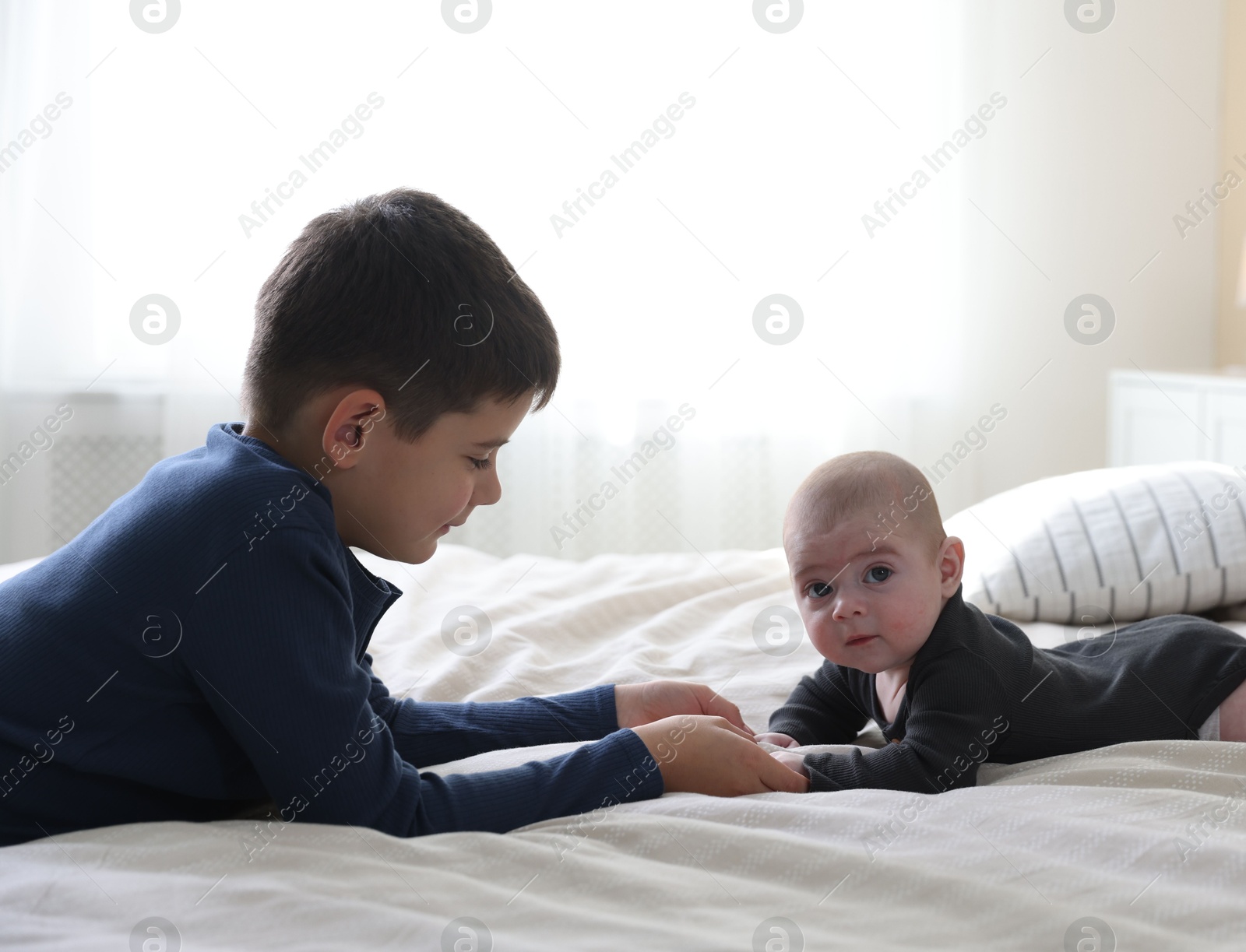 Cute little brothers holding hands on bed at home Photo of Cute little brothers holding hands on bed at home