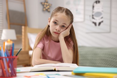 Photo of Dyslexia. Upset little girl reading book at table indoors