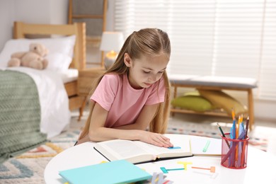 Photo of Dyslexia. Little girl reading book at table indoors