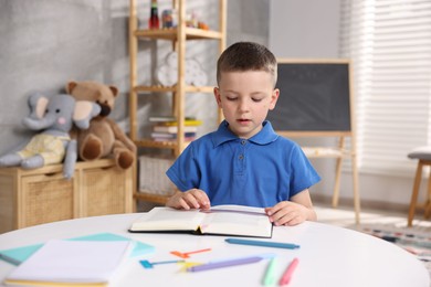 Photo of Dyslexia. Little boy reading book at table indoors
