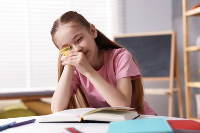 Photo of Dyslexia. Little girl reading book at table indoors