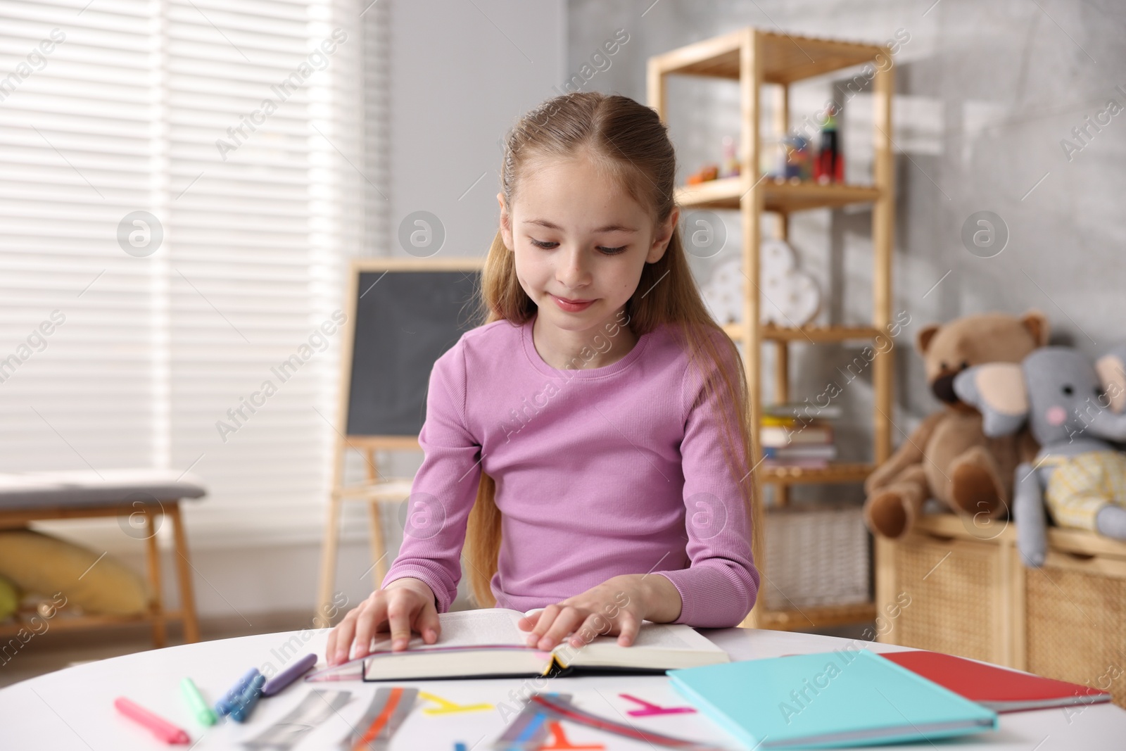 Dyslexia. Little girl reading book at table indoors Photo of Dyslexia. Little girl reading book at table indoors