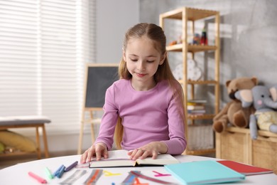 Photo of Dyslexia. Little girl reading book at table indoors