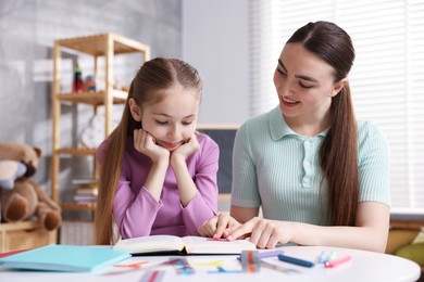 Photo of Dyslexia. Mother and her daughter reading book at table indoors