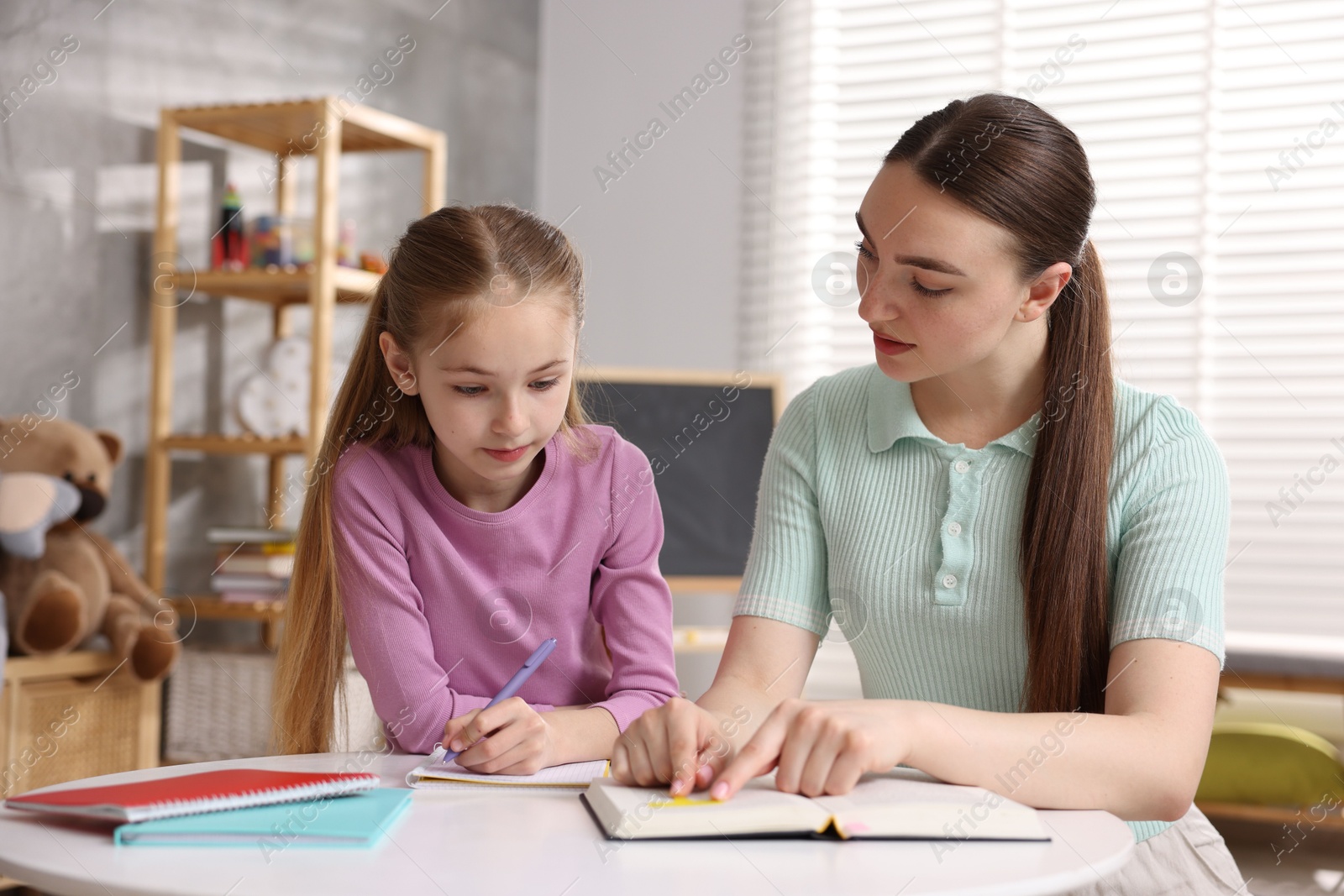Dyslexia. Mother with her daughter reading book and writing at table indoors Photo of Dyslexia. Mother with her daughter reading book and writing at table indoors