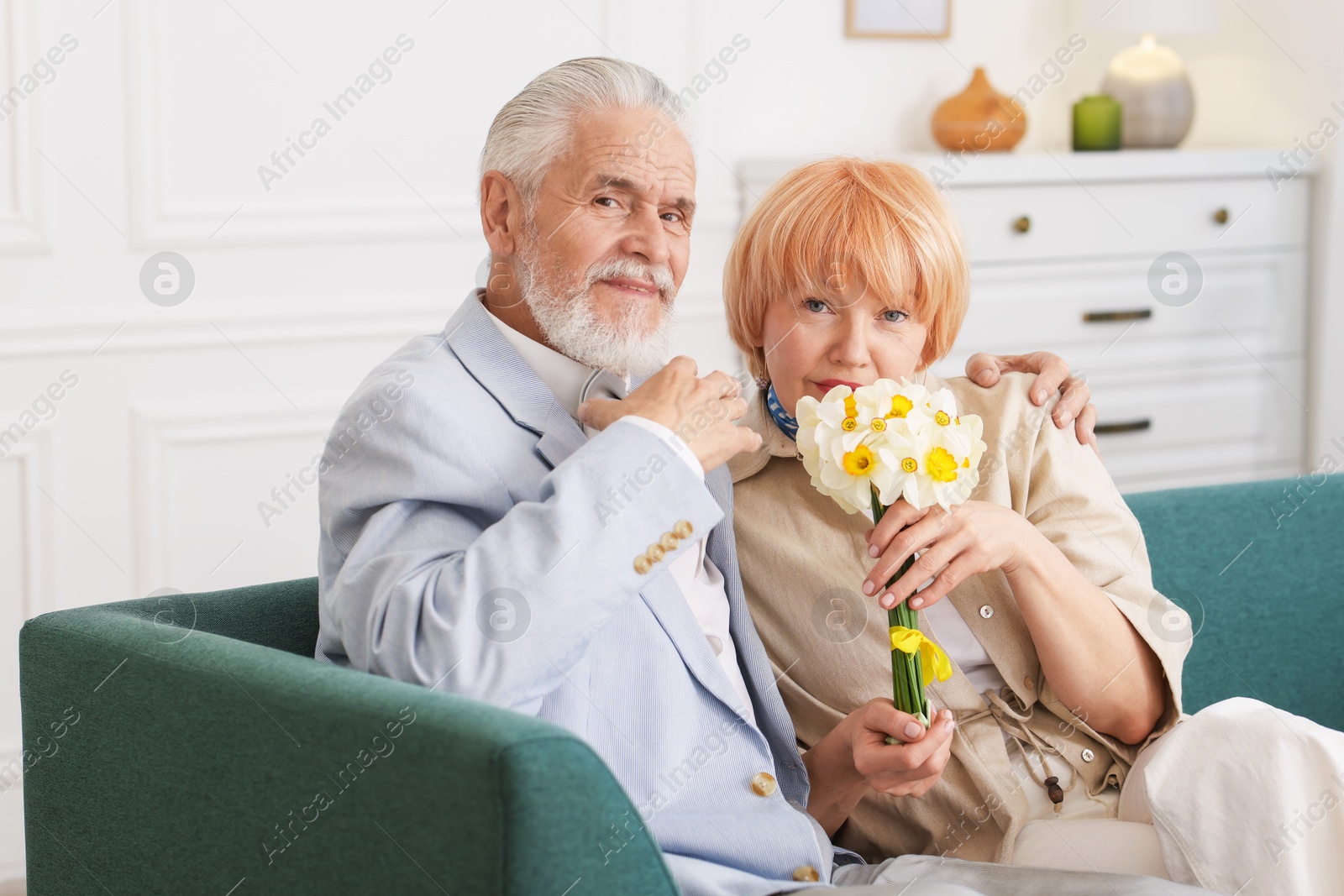 Lovely senior couple with bouquet of flowers on sofa at home Photo of Lovely senior couple with bouquet of flowers on sofa at home