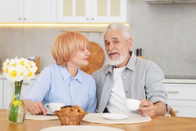 Photo of Lovely senior couple having breakfast together at wooden table in kitchen