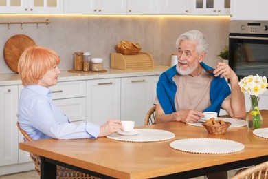 Photo of Lovely senior couple having breakfast together at wooden table in kitchen