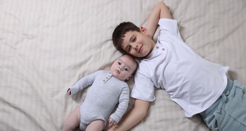 Photo of Cute little brothers on bed, top view. Space for text
