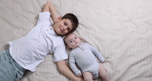 Photo of Cute little brothers on bed, top view. Space for text