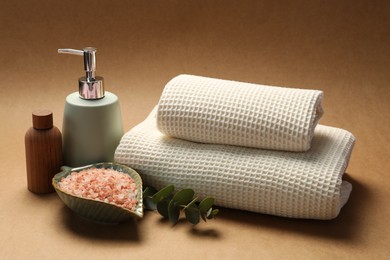 Photo of Clean waffle towels, sea salt, cosmetic products and eucalyptus branch on brown background