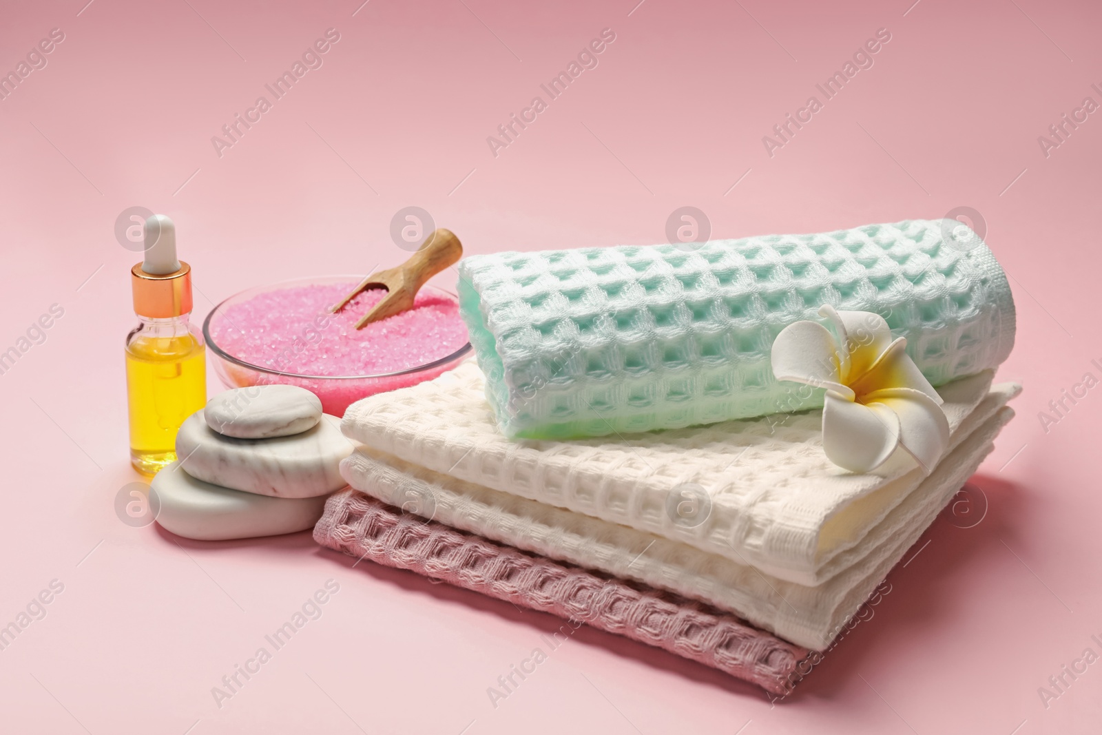 Clean waffle towels, cosmetic product, sea salt, spa stones and plumeria flower on pink background Photo of Clean waffle towels, cosmetic product, sea salt, spa stones and plumeria flower on pink background